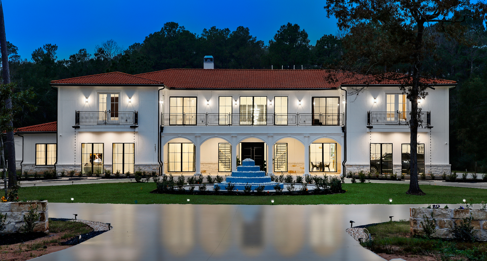 Full front elevation of the estate at twilight with illuminated arches and fountain